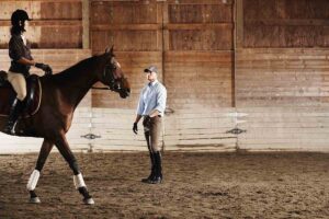 A horse trainer teaches a rider on a horse