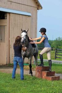 a young woman getting on a gray horse with a handler's help