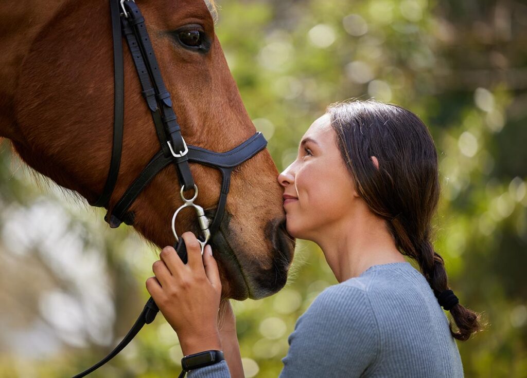 closeup of a young woman kissing her bay horse's nose