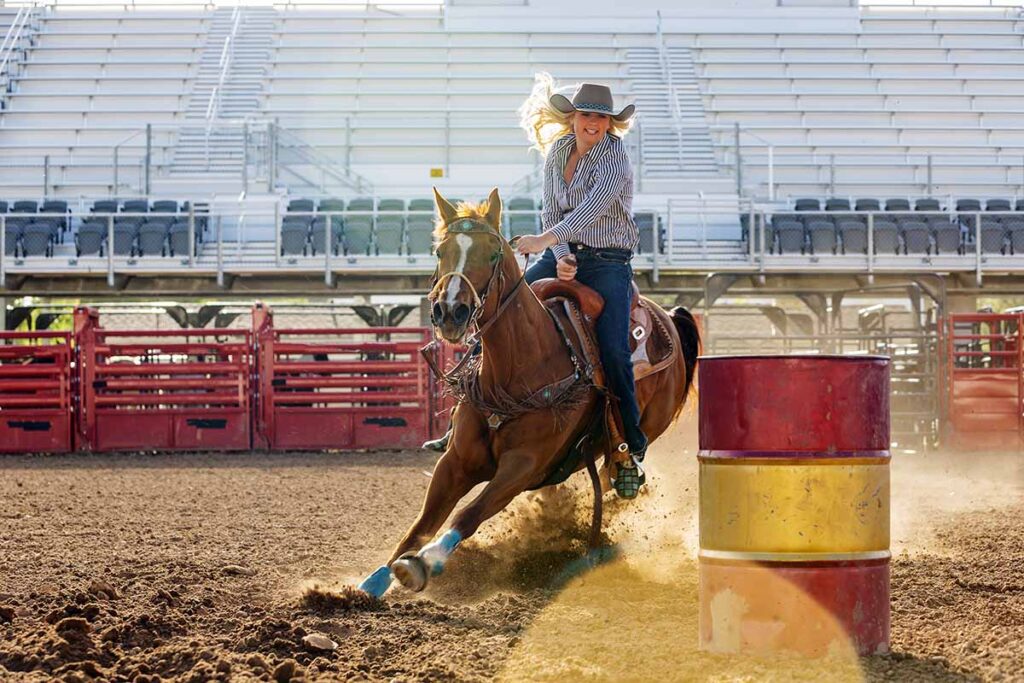 A woman turns a palomino horse quickly around a red and yellow barrel in a barrel racing event