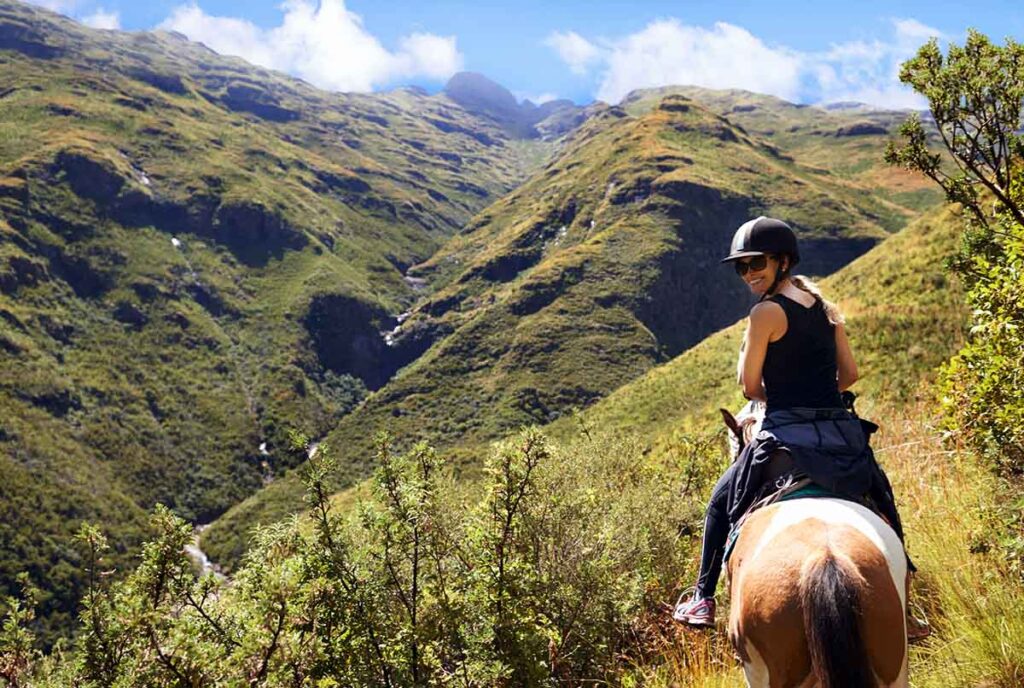A woman in a black top rides her paint horse along a dramatic cliffside trail.