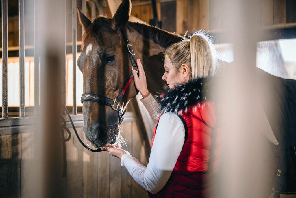 A woman calms a horse that pulls back when tied by using a quick-release knot to tie him to a stall grate.