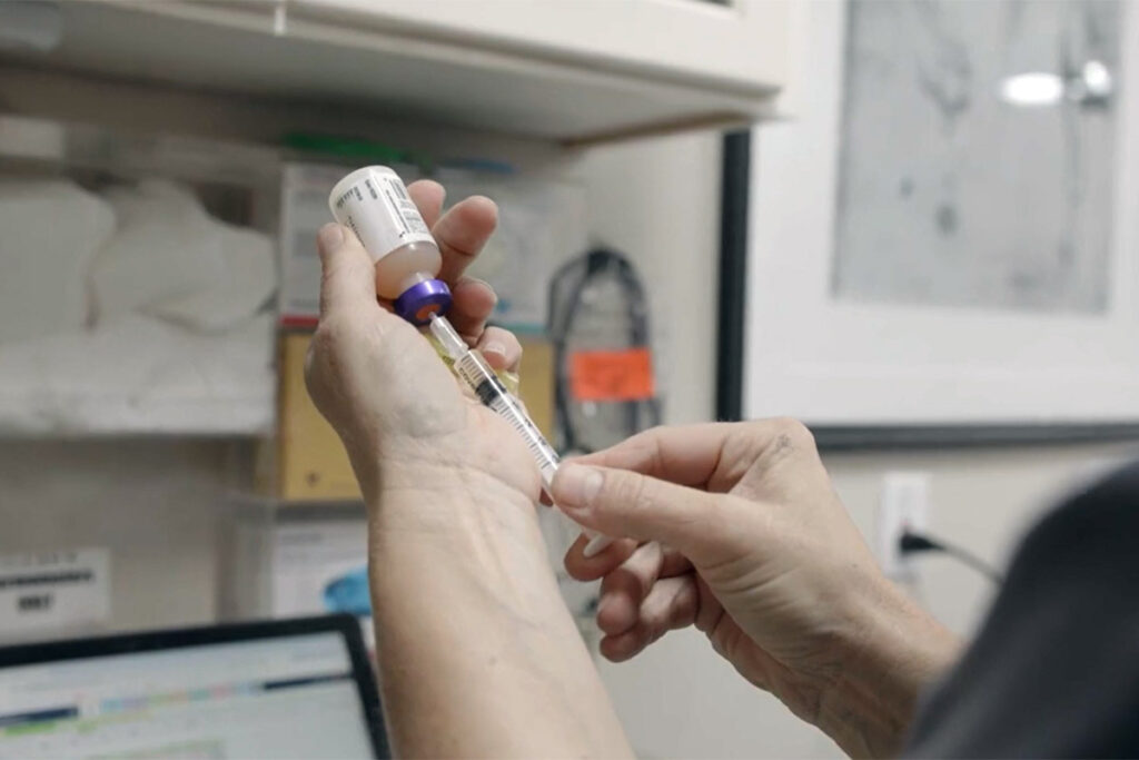 A veterinarian draws sedative into a syringe while discussing how owners can afford unexpected horse care expenses