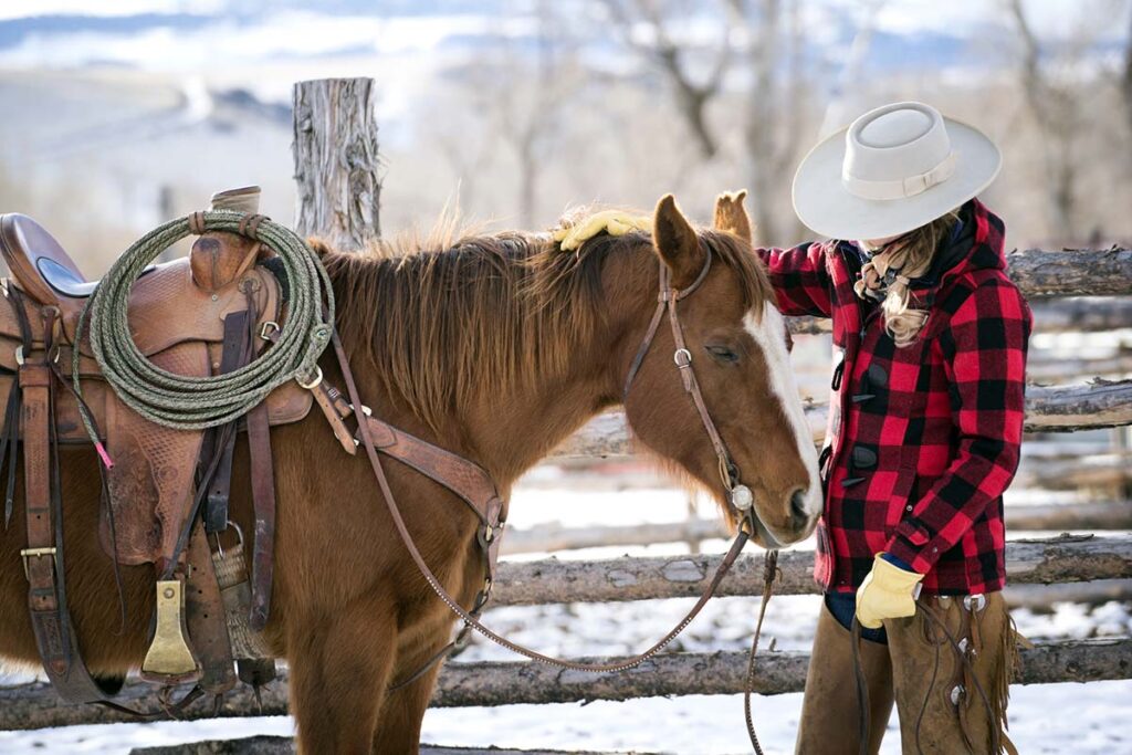 a cowgirl spends time petting her chestnut horse wearing western tack in the snow