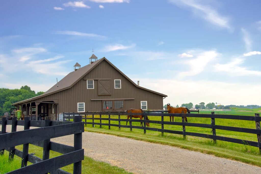 an affordable horse boarding facility with a gray barn and well-kept fenceline