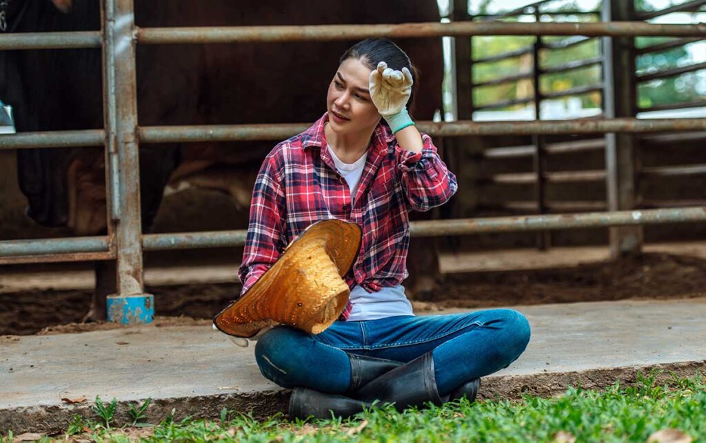 A woman on a farm sits down to take a break from chores because she's hot and tired