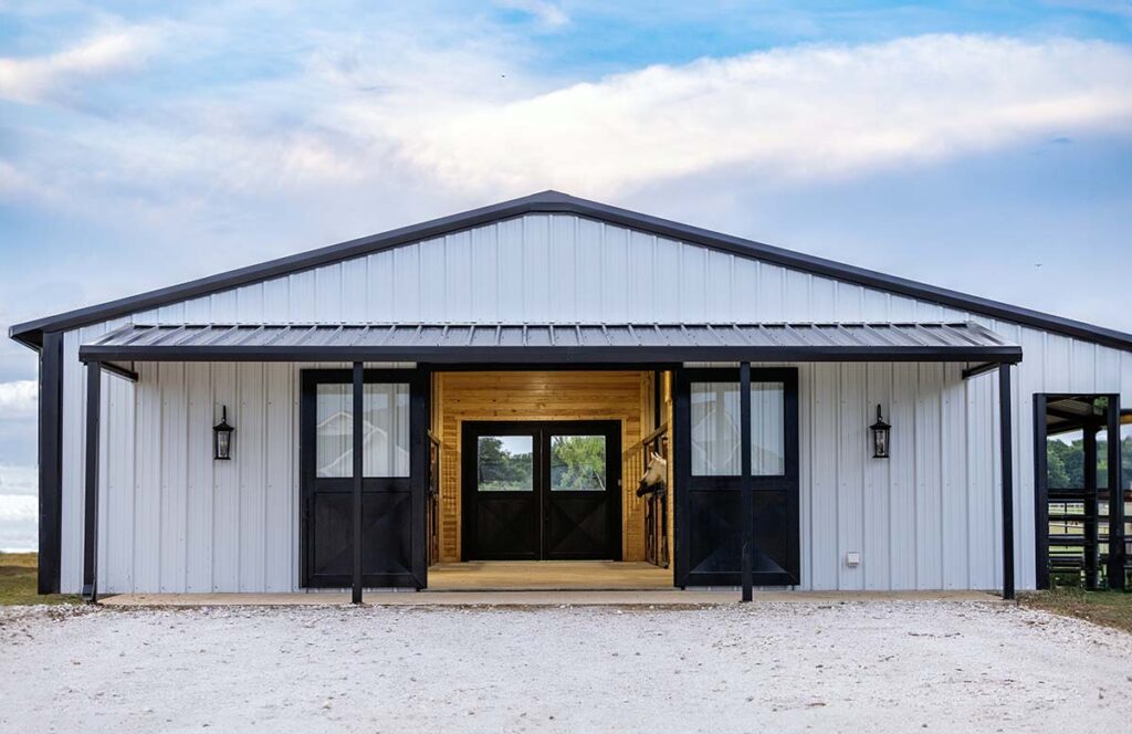 A clean and tidy white horse barn with doors open for an article about what not to store in horse barn.
