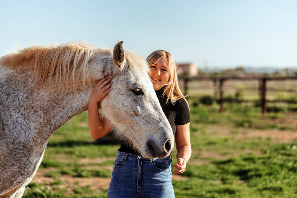 a woman provides aging horse care to a senior gray horse in a field