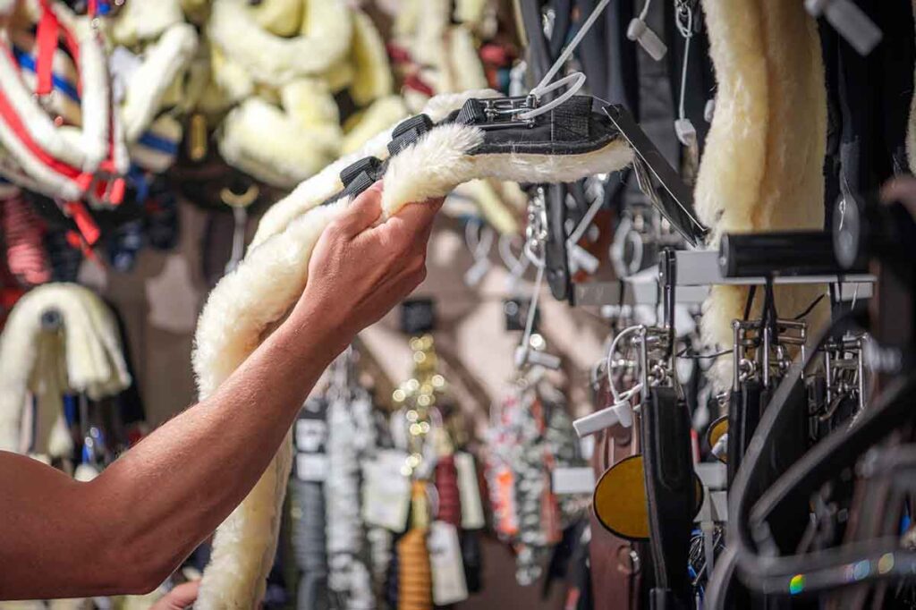 A horse owner looks for horse tack shopping tips while at a tack shop browsing the girth section.