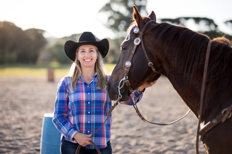 A cowgirl trying a horse before buying it stands in the arena with the bay western horse.