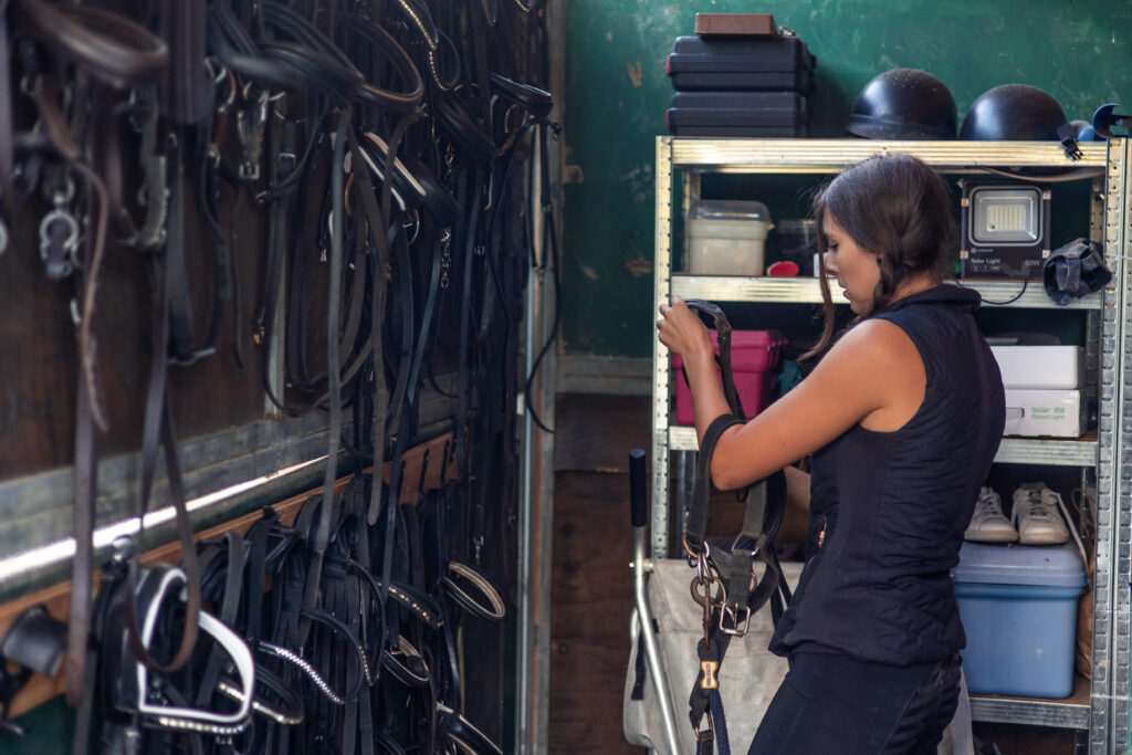 a woman organizes and hang her horse riding tack and bridles in a tack room