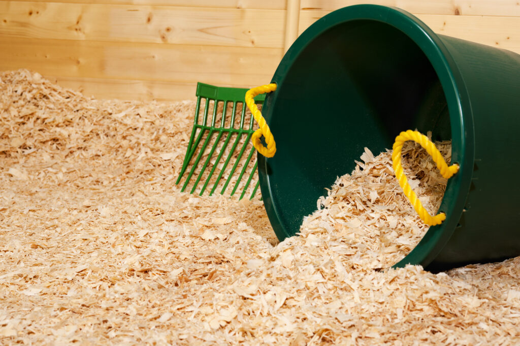 close-up image of shavings in a clean horse stall with a bucket and pitchfork